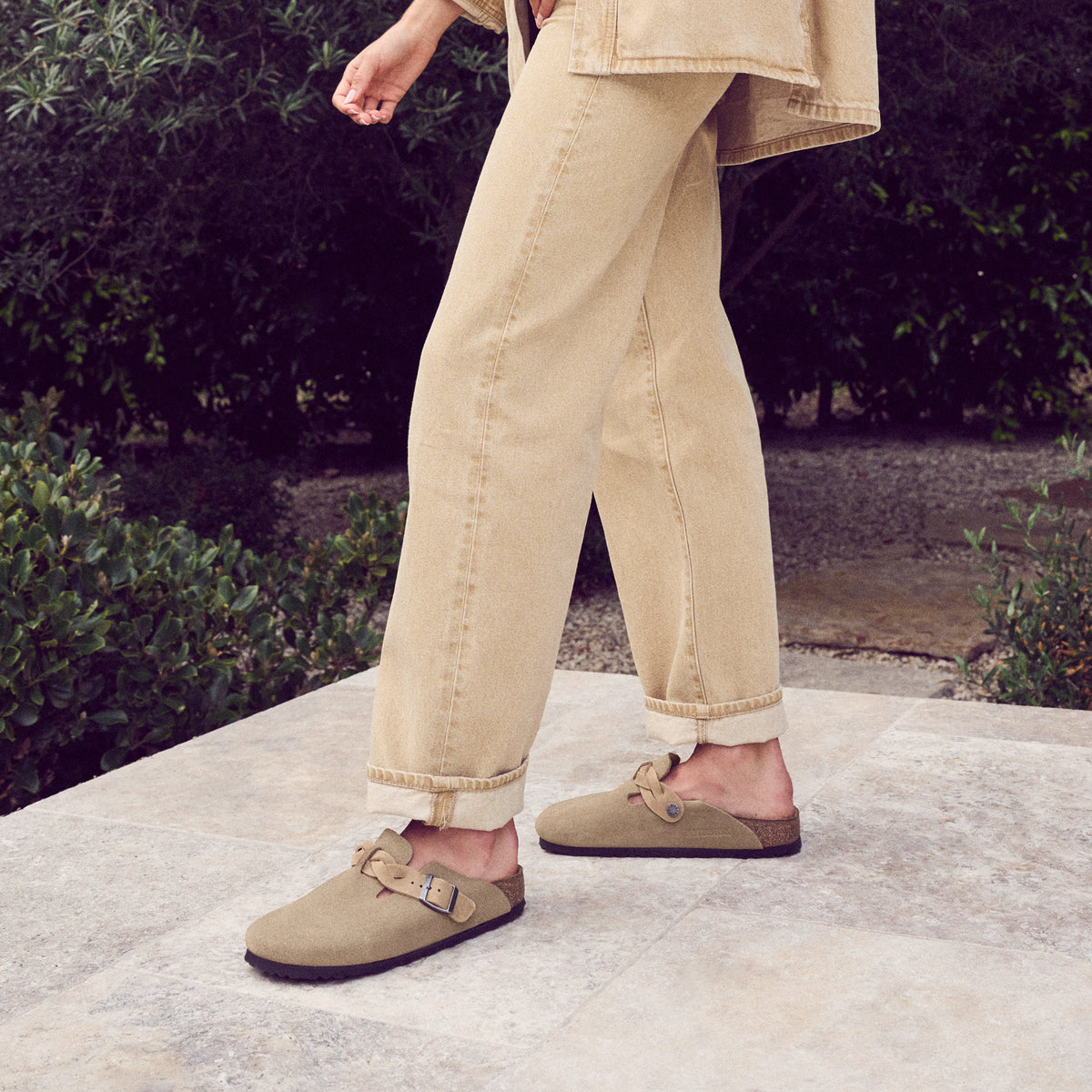 Woman wearing the boho-inspired braid Birkenstock Boston Braid in Taupe suede. Classic suede upper with a braided sophisticated strap resting on the Birkenstock original contoured footbed