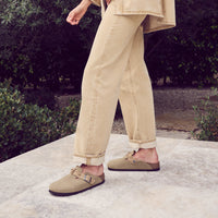 Woman wearing the boho-inspired braid Birkenstock Boston Braid in Taupe suede. Classic suede upper with a braided sophisticated strap resting on the Birkenstock original contoured footbed