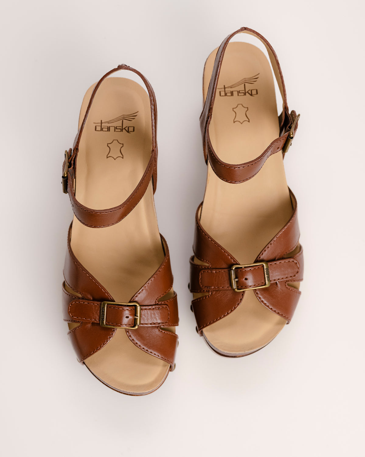 The Dansko Alanna in Tan leather is a standout piece from Dansko’s Ashland collection, designed for those who want a high-fashion silhouette without the usual discomfort of a tall heel. Every pair is handmade in Brazil, featuring a genuine wood wedge that has been hand-carved, sanded, and flame-burnished for a one-of-a-kind finish. The sculpted 3.5-inch heel is balanced by a 1.5-inch platform, creating a manageable 2-inch effective slope that provides height while maintaining stability.