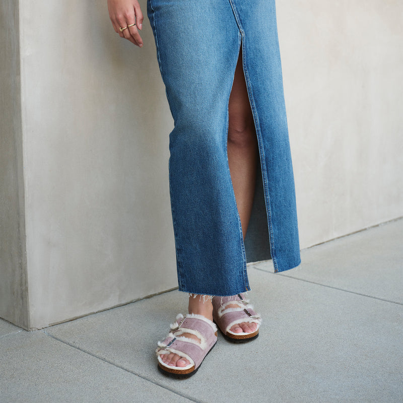 Woman wearing the Birkenstock Arizona sandal in Faded Purple featuring a soft genuine shearling lining, adjustable 2-strap design and cork and latex footbed. Wear it with or without socks!