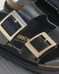 Black Birkenstock sandals with golden droplet buckles on a neutral background