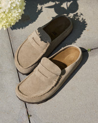 Pair of Birkenstock Naples Wrapped Clog in Taupe Suede on a concrete surface with flowers in the background