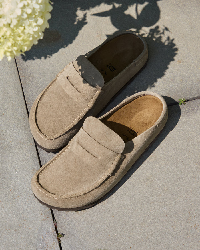 Pair of Birkenstock Naples Wrapped Clog in Taupe Suede on a concrete surface with flowers in the background
