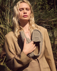 Woman holding a pair of Birkenstock Naples Wrapped Clogs in Taupe Suede against a natural background