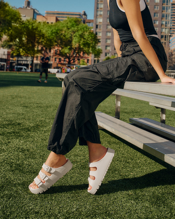 Person wearing black pants and Birkenstock EVA Florida Flex Platform Sandals in Eggshell sitting on a bench in an urban park.