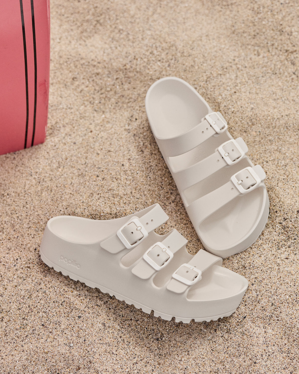 Birkenstock EVA Florida Flex Platform Sandals in Eggshell with three buckles on a sandy surface next to a pink bag.