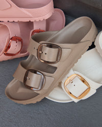 Beige, pink, and white Birkenstock EVA sandals with big buckles on a gray surface
