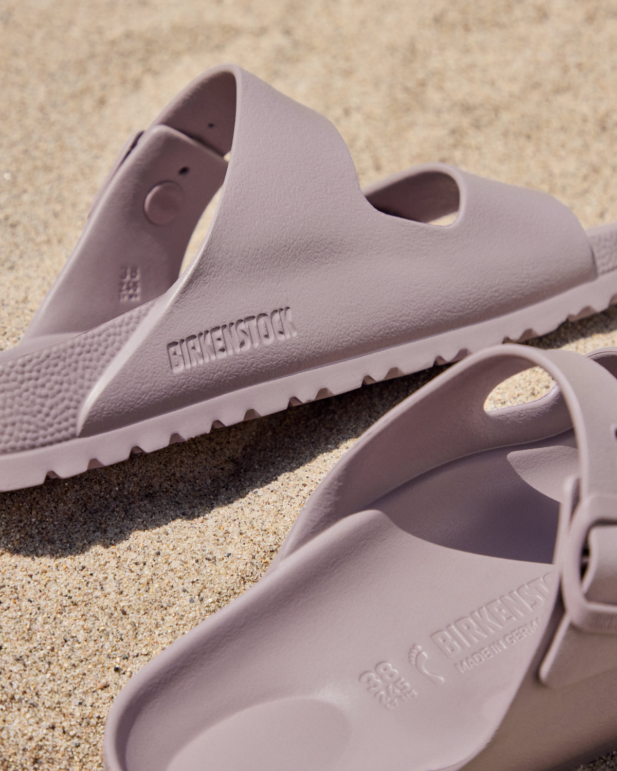 Pair of light purple Birkenstock EVA Arizona Faded Purple two-strap water-ready sandals on a sandy surface with 'Birkenstock' branding.