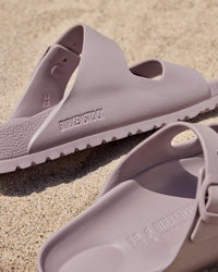 Pair of light purple Birkenstock EVA Arizona Faded Purple two-strap water-ready sandals on a sandy surface with 'Birkenstock' branding.