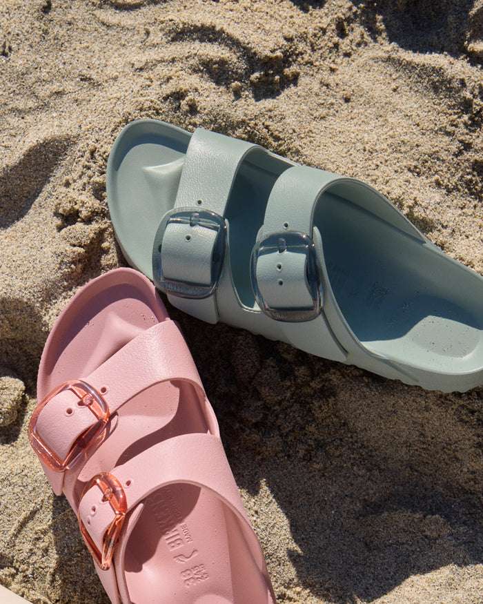 Pink and pure sage Birkenstock EVA Big Buckle sandals on a sandy beach