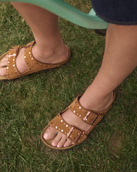 Mink brown Birkenstock sandals with rose-gold stud rivets and buckles on grass