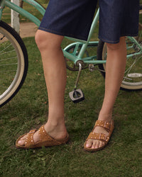 Person wearing Mink brown Birkenstock Arizona double-strap sandals with studs standing on grass next to a teal bicycle.