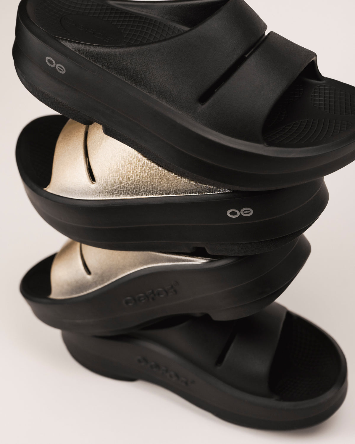 Stack of black and Latte golden OOFOS platform sandals on a light background
