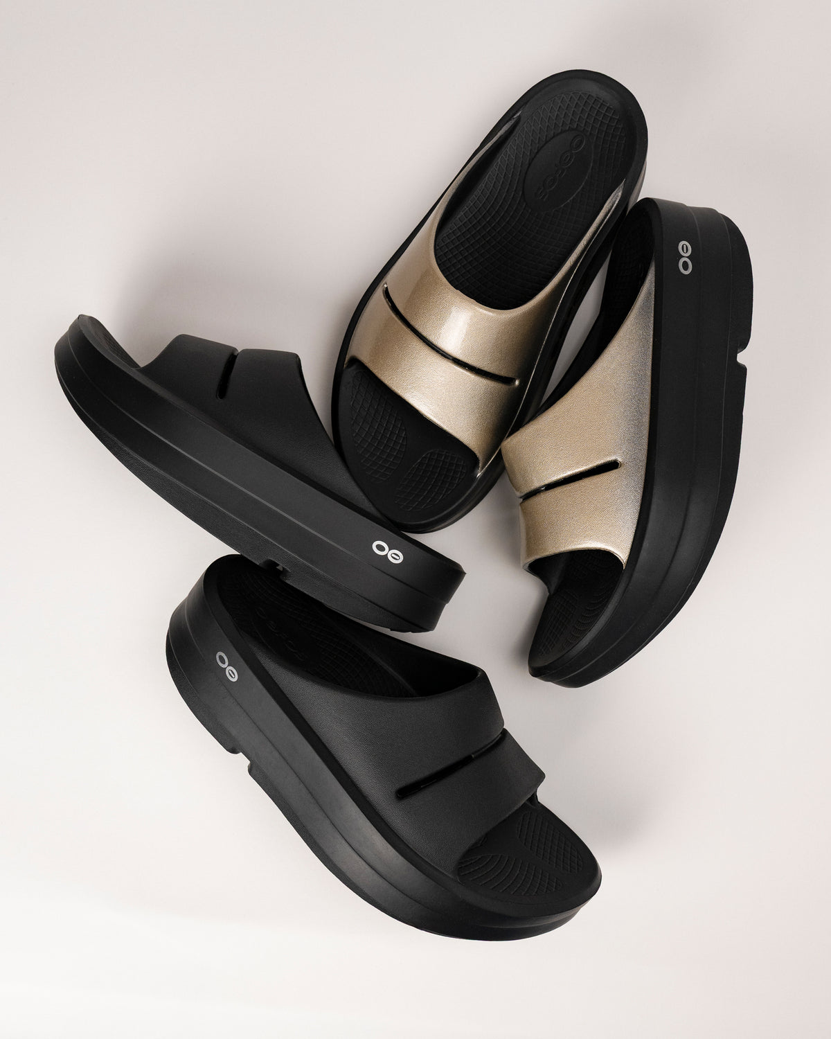 Black and gold OOFOS platform recovery slide sandals on a light background