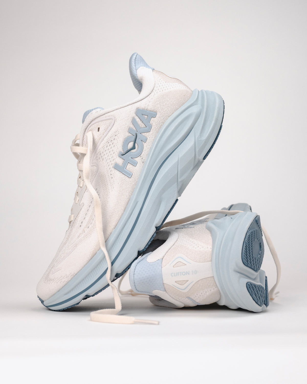 Pair of white and light blue sneakers with 'HOKA' branding on a light background