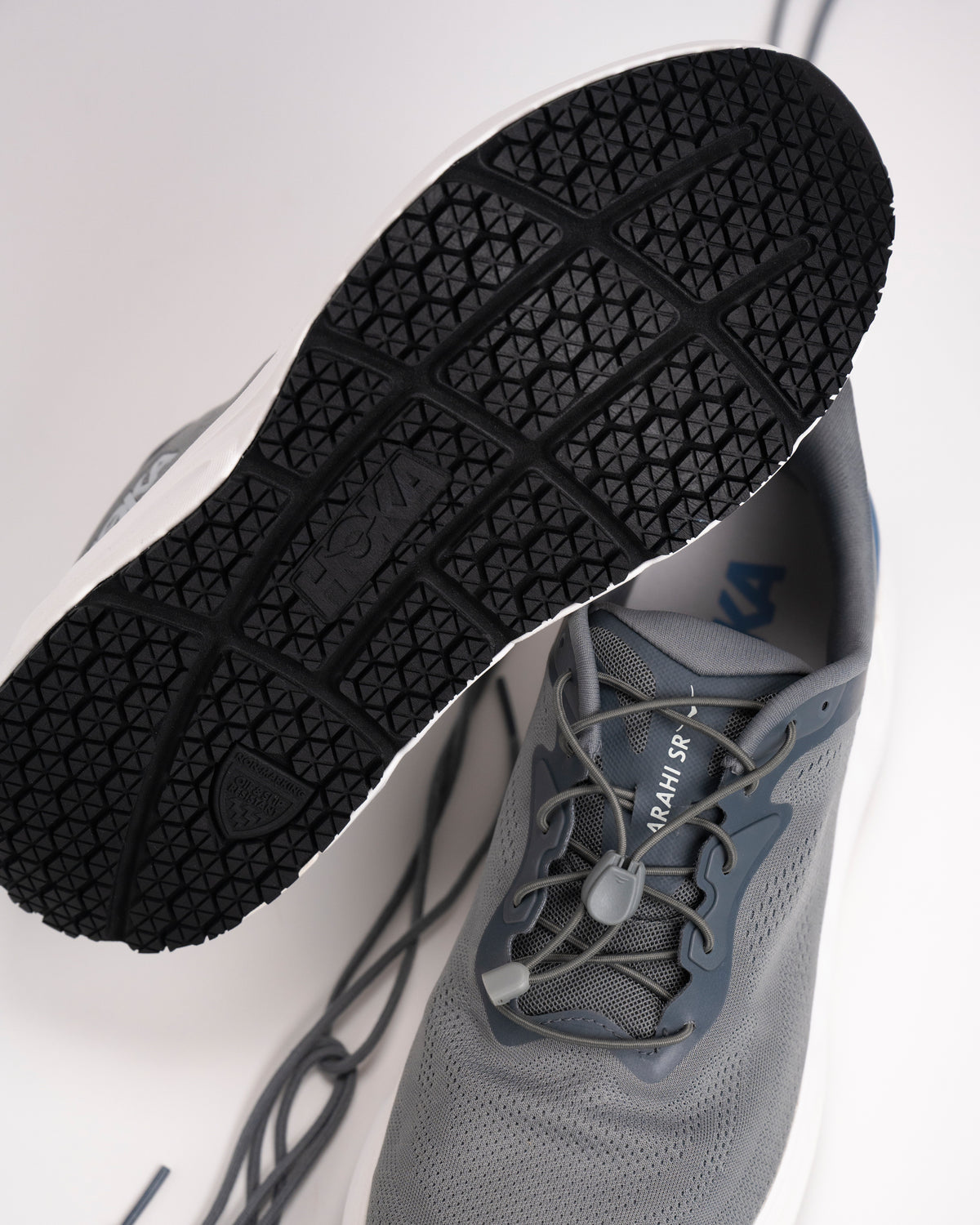 Detail view of the non-marking oil & slip resistant outsole and easy-on toggle lace design of the men's HOKA Arahi SR.