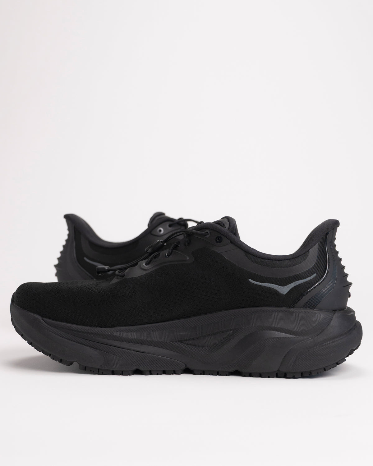 Side view of Men’s HOKA Arahi SR in Black showing slip-resistant rubber outsole and mild stability reinforced heel. 