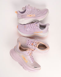 Women's HOKA Gaviota 6, Clifton 10, and Bondi 9 in Lilac purple colorway with orange peachy highlights. Cushioned running shoes for women.