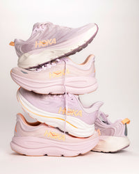 Women's HOKA Gaviota 6, Clifton 10, and Bondi 9 in Lilac purple colorway with orange peachy highlights. Cushioned running shoes for women.