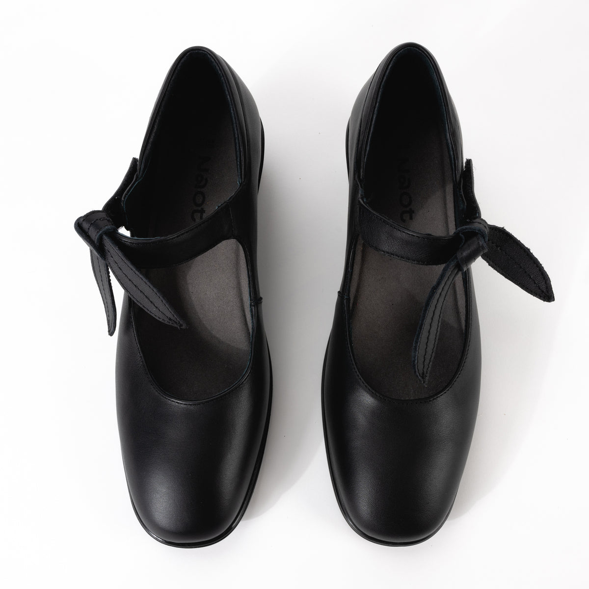 Top-down view of the Nobility Mary Jane from Naot in smooth black leather, highlighting the single strap across the instep with a removable leather bow, cushioned insole padding and heel along with a classic rounded toe design.