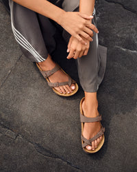 Young woman wearing brown Birkenstock Mayari Sandal in Mocha Birkibuc on a dark stone surface