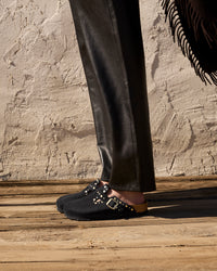 Lifestyle side profile shot highlighting the riveted strap and contoured footbed styled with leather pants and shawl.