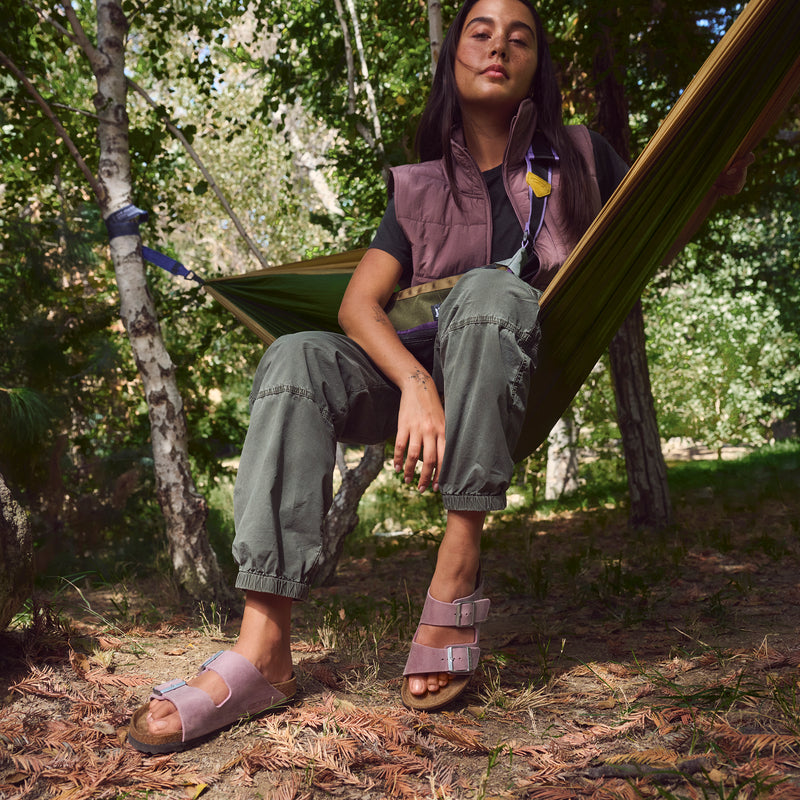 Female wearing the comfortable Lavender oiled leather two-strap Arizona sandal by Birkenstock, featuring a silvery buckle and unique oiled leather patina. 