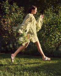 Woman in a light green dress walking outdoors with greenery in the background wearing Birkenstock Sydney Luxe Buckle sandal in Graceful Pearl White
