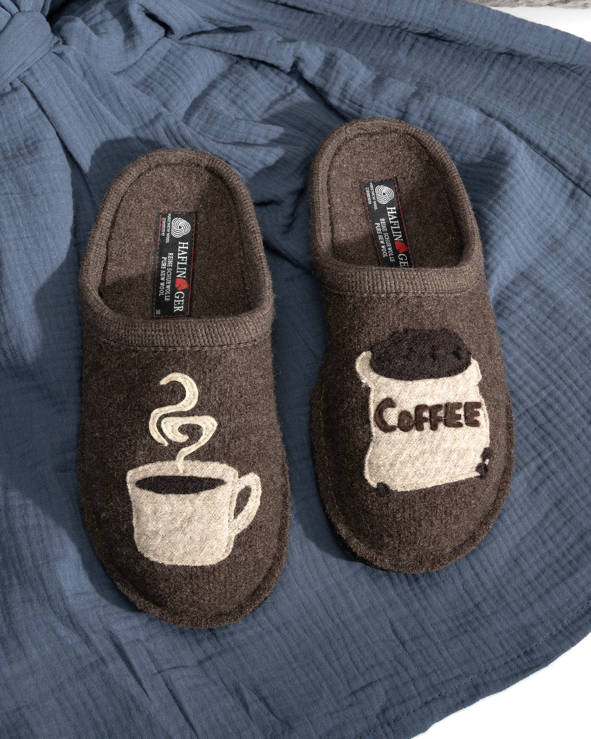 Brown Haflinger boiled wool slippers with coffee-themed design on a blue fabric background 313039-63