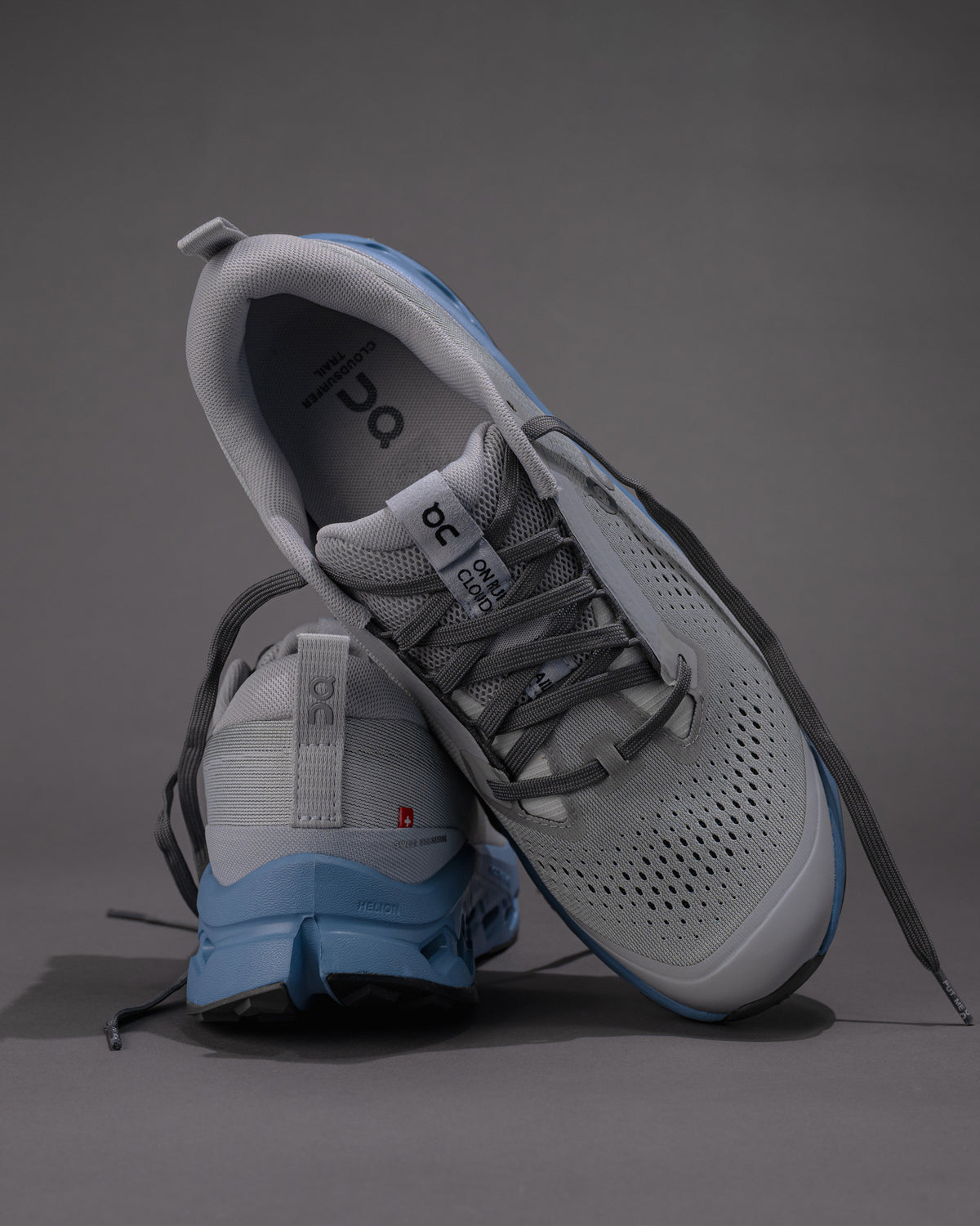 Gray and blue athletic shoes on a gray background. Men's On Cloudsurfer Trail 2 in Rock/Niagara – Plush Cushioning Trail Running Shoe