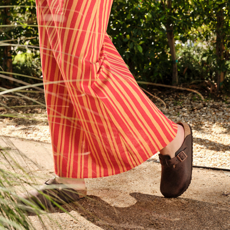 Lifestyle shot of a female wearing the Birkenstock Boston Clog in Habana Oiled Leather, a Unisex slip-on clog with an adjustable strap for the perfect fit.