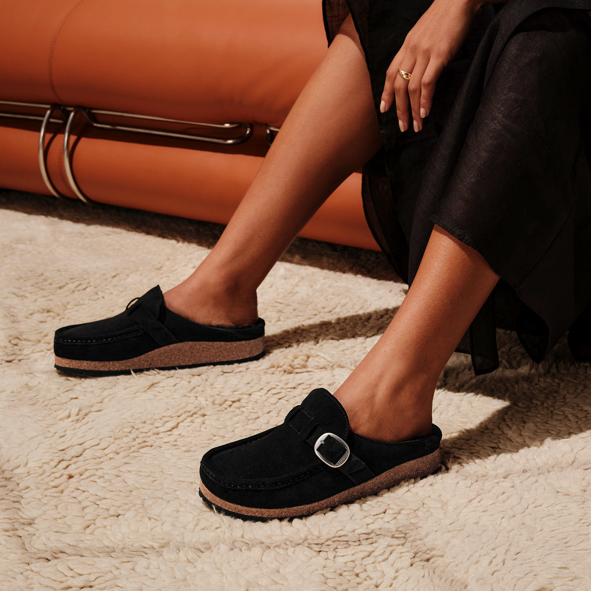 Woman wearing the Birkenstock Buckley with genuine Shearling lining in soft suede black. Matte silver hardware detail and adjustable strap.