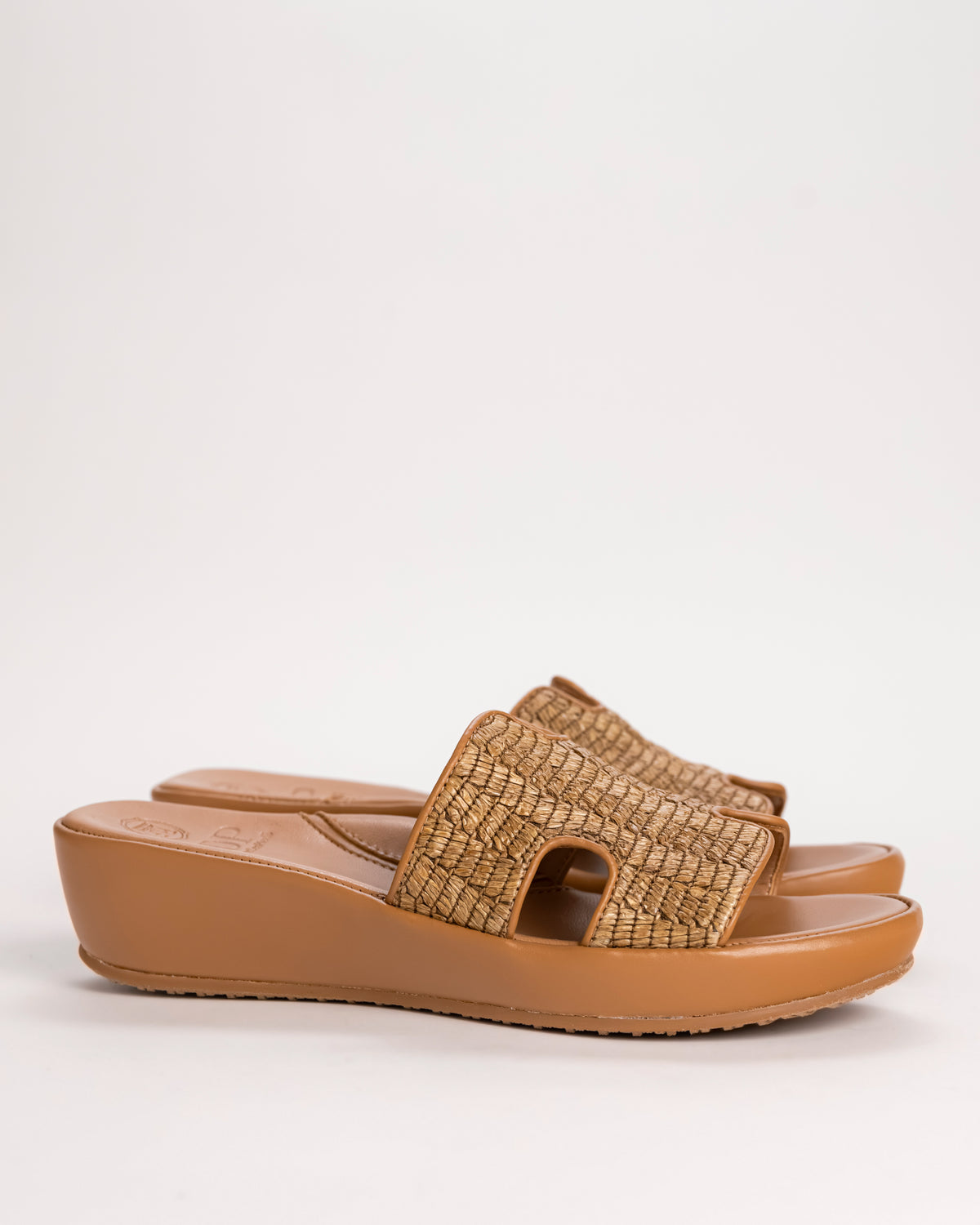 L’Amour Des Pieds Catian Slide sandal in brown woven raffia on white background.