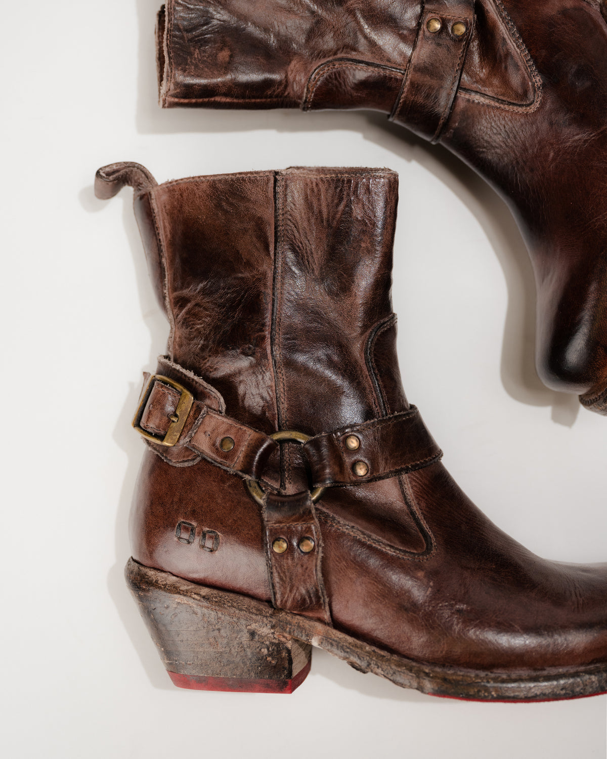 Close‑up of antique metal ring and leather harness strap on Bed|Stü Homage boot