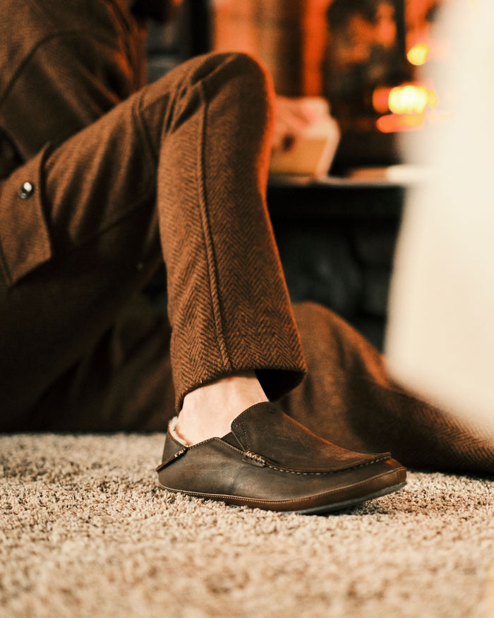 Person wearing brown pants and dark shoes sitting on a carpeted floor.