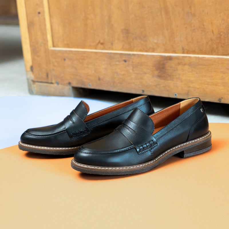 Close up view of ALDAYA Penny Wide black leather loafers featuring a sleek calfskin leather upper, extra wide fit, and 3 cm thick synthetic sole. Classic penny loafer design with a modern twist, perfect for pairing with skirts, trousers, or dresses. Extra comfort with a removable insole and soft pigskin-textile lining.