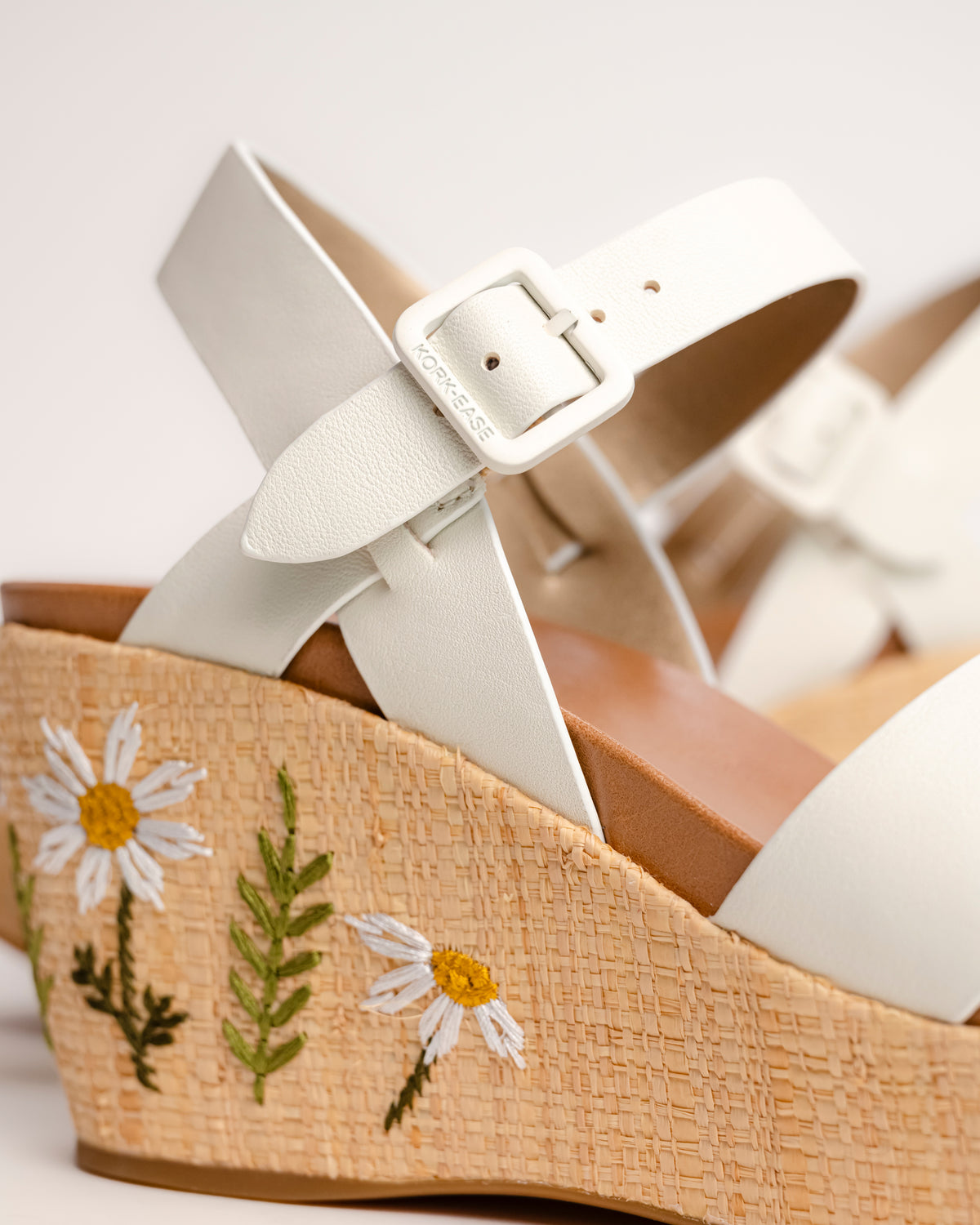 The Ava 2.0 in White / Cream with Floral Embroidery is a modernized tribute to the legendary 1970s "Buffalo Sandal" that put Kork-Ease on the fashion map. This specific edition pairs smooth, cream-colored leather straps with a beautifully textured raffia-wrapped wedge, featuring delicate, multi-colored floral embroidery for a soft, bohemian touch. It’s a design that feels both nostalgic and fresh, offering a substantial platform look that doesn't feel heavy or clunky.