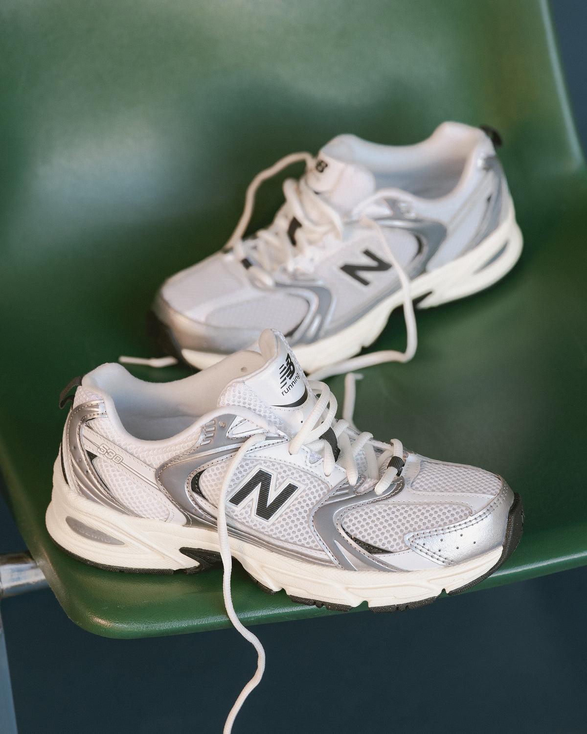 Pair of white and gray New Balance 530 sneakers on a green chair