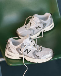 Pair of white and gray New Balance 530 sneakers on a green chair