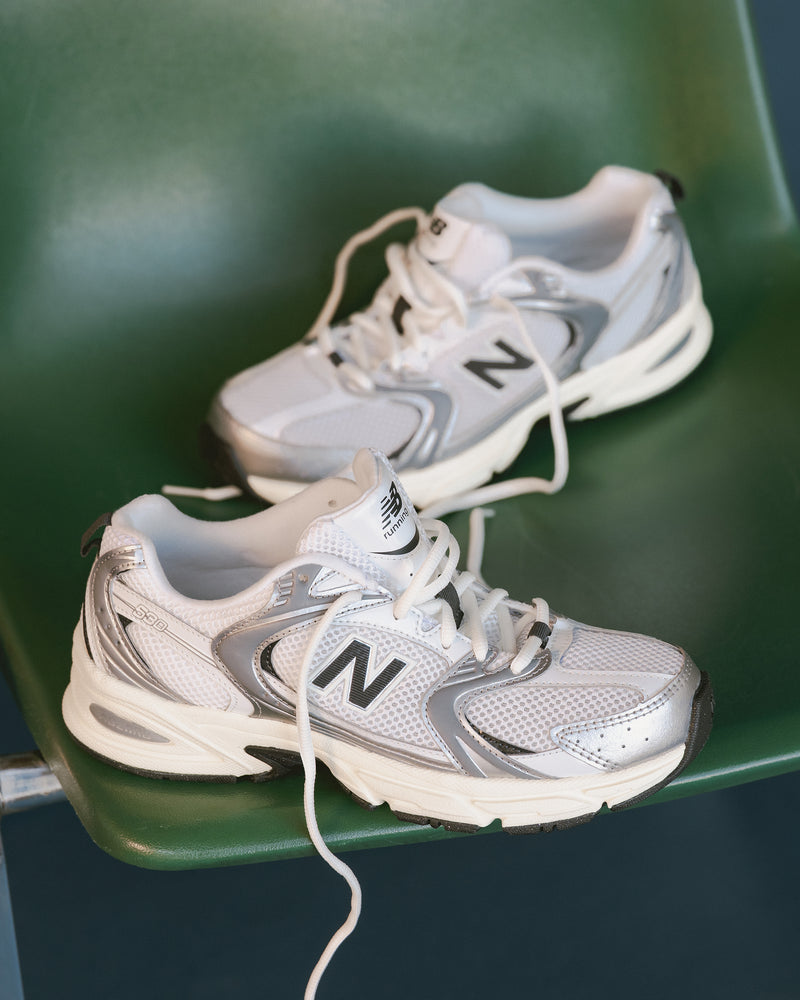 Pair of white and gray New Balance 530 sneakers on a green chair