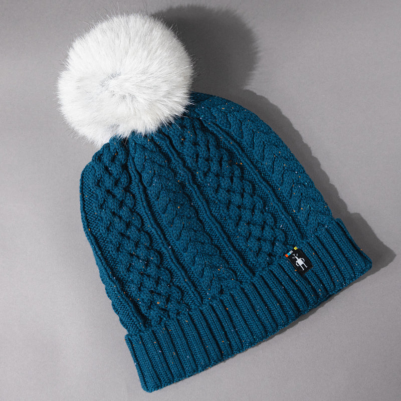 Overhead detail view of the Women's Smartwool Lodge Girl Soft Merino Knit Beanie with Faux Fur Pom in Twilight / teal blue