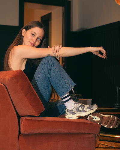 Woman sitting on a red couch wearing blue jeans and New Balance 530 v1 sneakers.
