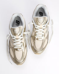A New Balance 603 sneaker in metallic gold and beige with white laces and a chunky white and beige sole, shown from a side profile on a light gray background. W60347S 