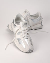 Angled front view of women’s New Balance 327 sneaker in Silver metallic showing laces and nylon tongue
