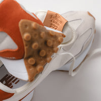 Detailed shot of the back logo patch on the tongue of the New Balance 327 V1 in Rust and Sea Salt, reading "The Intelligent Choice 327"